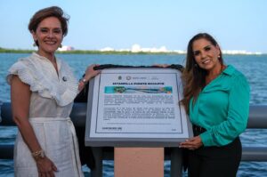 Mara Lezama y Violeta Abreu sostienen la placa conmemorativa de la estampilla postal del Puente Nichupté durante la ceremonia en Cancún.