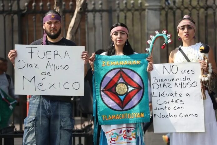 Protesta de representantes de pueblos originarios frente a la visita de la presidenta madrileña Isabel Díaz Ayuso, con carteles que exigen “Fuera Díaz Ayuso de México”
