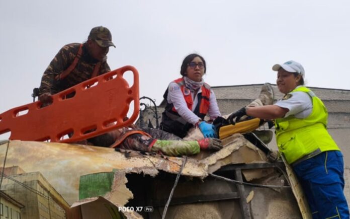 Rescatistas y paramédicos auxiliando a un herido sobre la carrocería destrozada de un autobús de pasajeros, después de que un muro colapsara sobre el vehículo en la calle Allende del Centro Histórico.