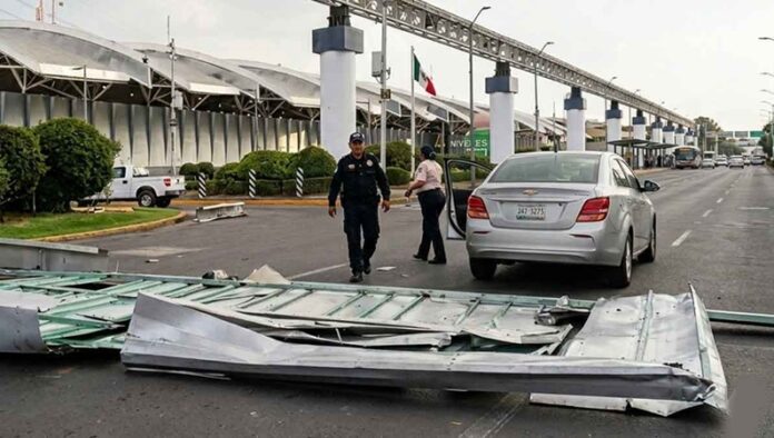 Restos de una estructura metálica desprendida bloquean parcialmente la vialidad frente a la Terminal 1 del AICM, mientras policías atienden a una conductora afectada junto a su vehículo.