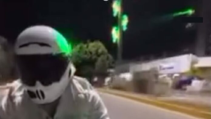 Motociclista circula sobre la Vía Atlixcáyotl mientras un rayo láser verde apunta hacia la vialidad durante los ataques investigados en Puebla.