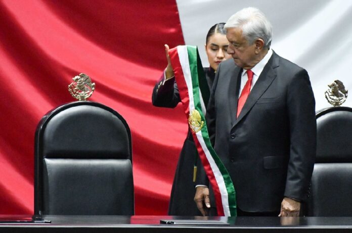 Andrés Manuel López Obrador durante una ceremonia oficial frente a una gran bandera de México en el recinto legislativo.