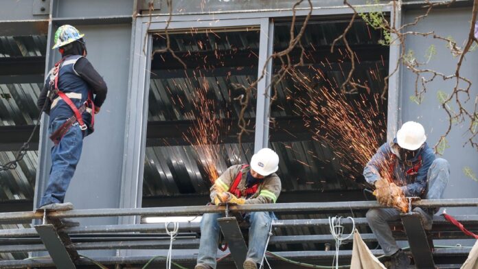 Trabajadores de la construcción realizan labores de soldadura y corte sobre una estructura metálica en altura.