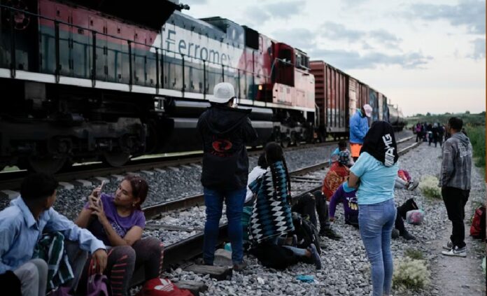 Migrantes esperan junto a una vía férrea mientras un tren de carga avanza, una escena que ilustra las rutas utilizadas durante el tránsito irregular hacia la frontera con Estados Unidos.