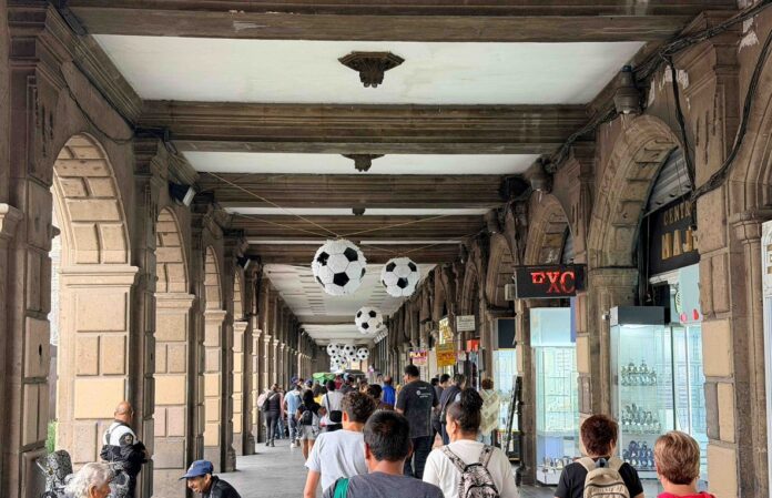 Personas caminan bajo un corredor del Centro Histórico decorado con balones gigantes de futbol rumbo al Mundial 2026.