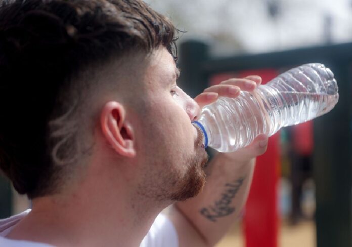 Hombre bebe agua de una botella plástica desechable durante un día caluroso, en medio del debate por las nuevas reglas de hidratación rumbo al Mundial 2026.