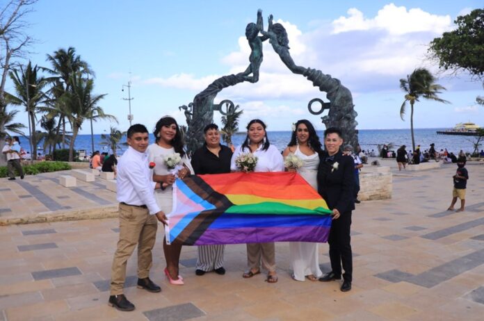 Parejas de la comunidad LGBTTTIQA+ posan con la bandera de la diversidad sexual en Playa del Carmen, en el marco de las bodas igualitarias impulsadas por el gobierno municipal encabezado por la presidenta Estefanía Mercado.