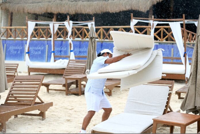 Empleado acomoda camastros en una zona de playa de Quintana Roo durante la temporada baja, periodo en el que hoteles aplican esquemas de días solidarios para evitar despidos.