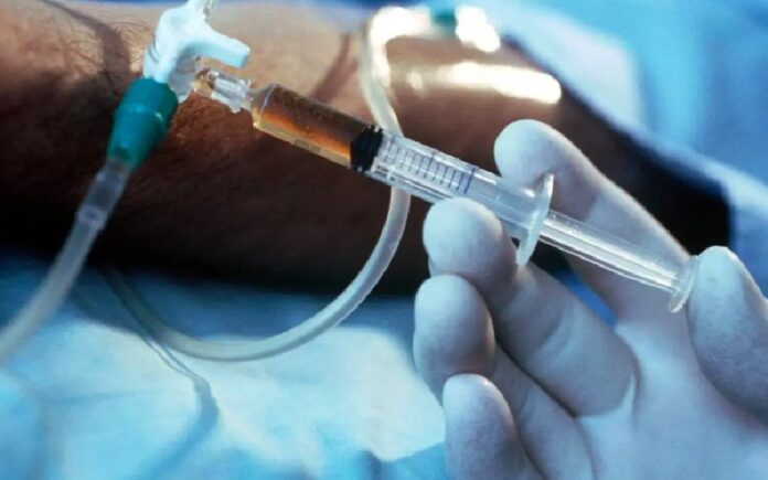 Personal médico sostiene una jeringa conectada a una vía intravenosa durante un procedimiento hospitalario relacionado con cuidados al final de la vida.