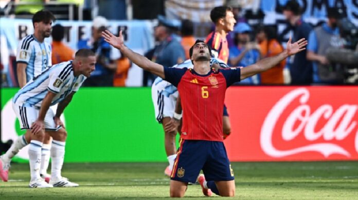 Un futbolista de España celebra de rodillas con los brazos abiertos mientras jugadores de Argentina muestran su desilusión.