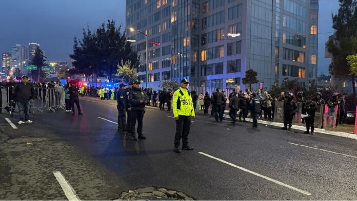 Policías resguardan una avenida frente al hotel de concentración de Inglaterra mientras aficionados permanecen detrás de vallas metálicas.