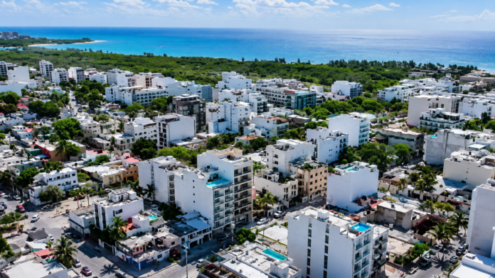 Vista aérea de edificios residenciales y comerciales de Playa del Carmen con el mar Caribe al fondo.