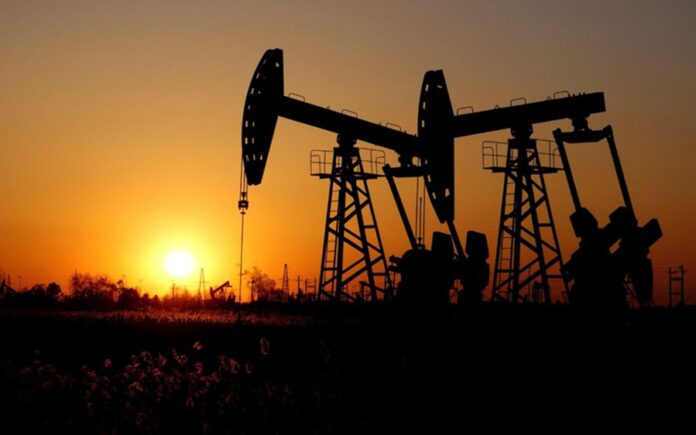 Bombas extractoras de petróleo operan al atardecer en un campo petrolero con siluetas industriales.