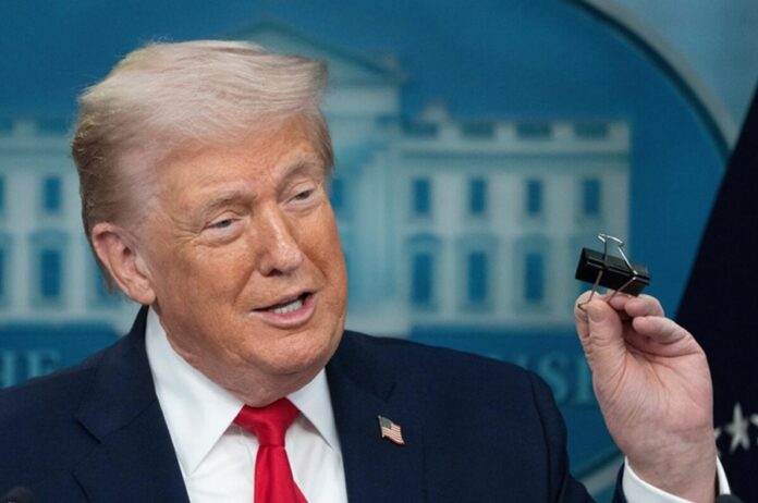 Donald Trump habla durante una conferencia mientras sostiene un clip metálico con la mano.