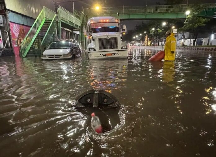 Vehículos parcialmente inundados y un trabajador de emergencia durante una fuerte inundación ocasionada por la tormenta del miércoles en la Ciudad de México.