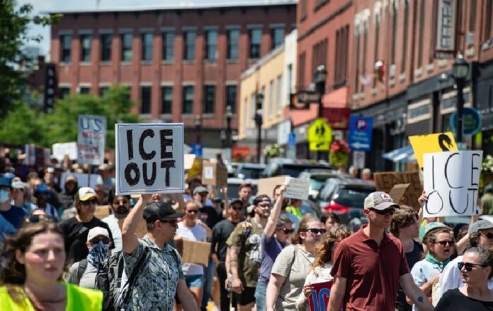 Manifestantes marchan por una calle con pancartas que muestran el mensaje ICE OUT durante una protesta contra las autoridades migratorias.