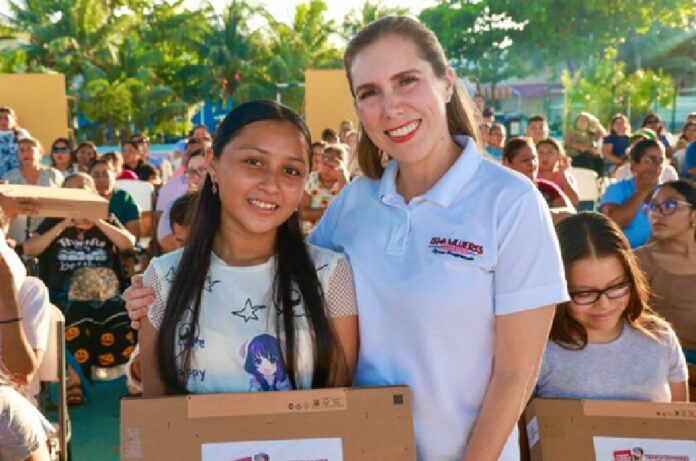 Atenea Gómez Ricalde posa junto a una estudiante durante una entrega de apoyos con personas reunidas al fondo.