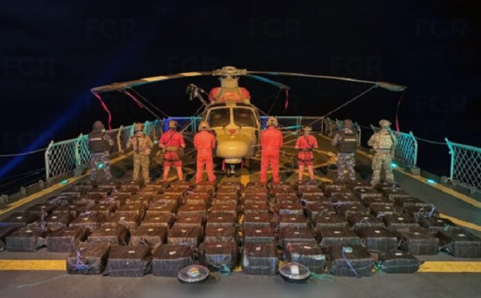 Elementos de la Marina custodian paquetes asegurados de cocaína frente a un helicóptero sobre la cubierta de una embarcación durante un operativo nocturno.
