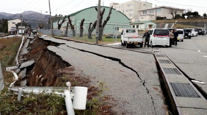 Carretera con profundas grietas y hundimientos junto a varios vehículos y personas tras daños provocados por un sismo en Japón.