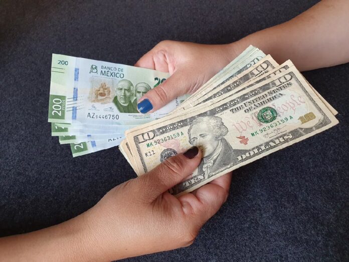 Dos personas sostienen billetes de dólares estadounidenses y billetes mexicanos de 200 pesos.