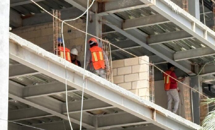 Trabajadores de construcción con chalecos de seguridad dentro de una obra con estructura metálica en proceso de edificación.