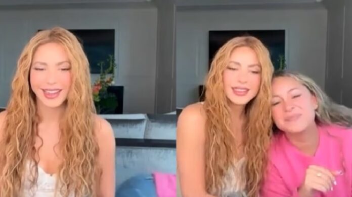 Shakira durante una videollamada sonríe mientras su asistente aparece detrás de ella durante una entrevista.
