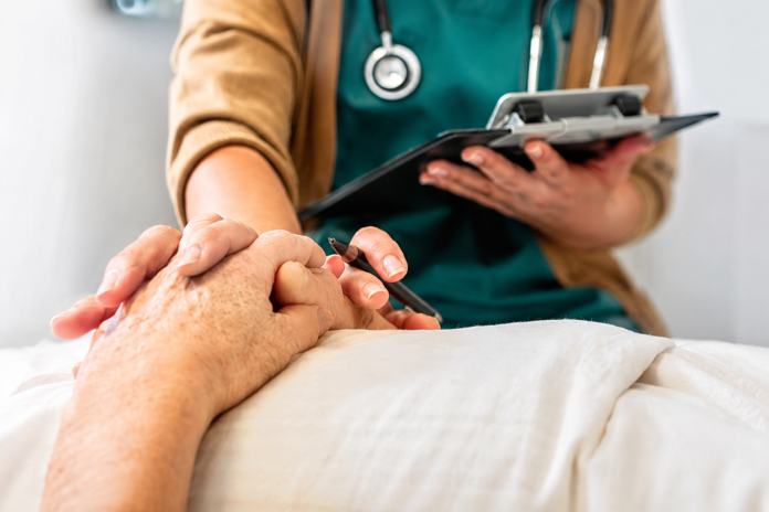 Profesional de la salud sostiene la mano de un paciente mientras sostiene una tableta electrónica durante una consulta médica.