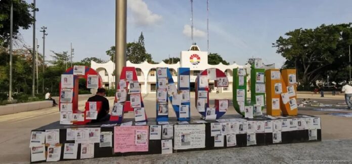 Fichas de búsqueda de personas desaparecidas colocadas sobre las letras monumentales de Cancún durante una jornada organizada por el colectivo Verdad, Memoria y Justicia.