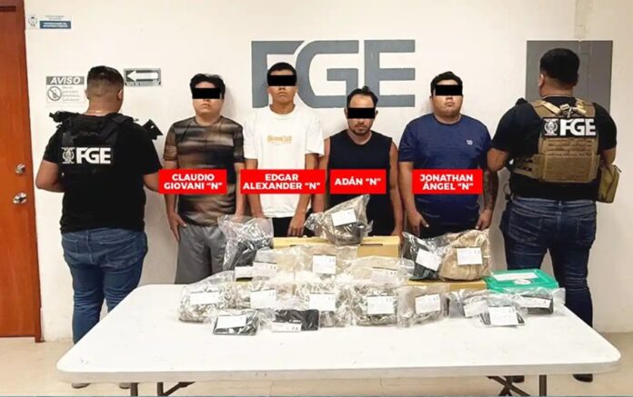 Elementos de la Fiscalía General del Estado presentan a cuatro detenidos junto a bolsas con presunta droga asegurada sobre una mesa.