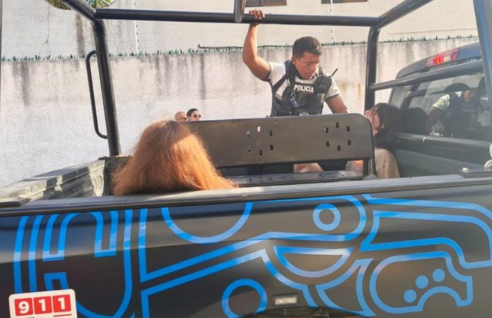 Elemento de la Policía Turística custodia a personas detenidas en la parte trasera de una patrulla en Playa del Carmen.