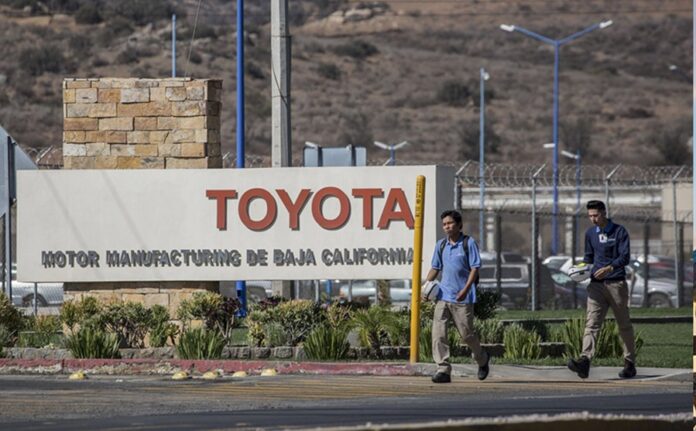 Entrada de la planta Toyota Motor Manufacturing de Baja California mientras trabajadores caminan frente al acceso principal.