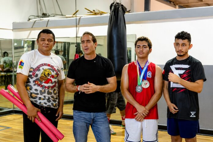 Diego Castañón Trejo junto a integrantes de la academia de box y al atleta Emiliano López dentro de un gimnasio de la Unidad Deportiva de Tulum.