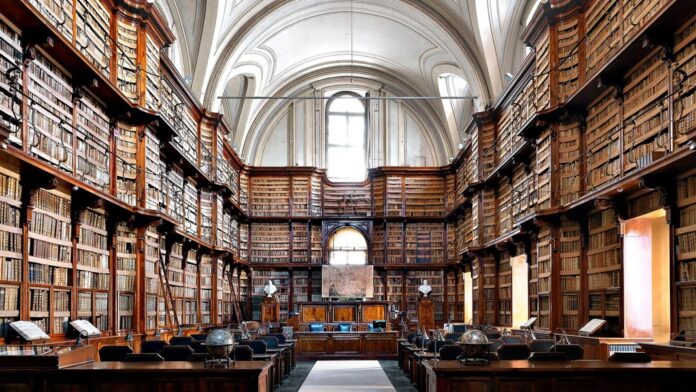 Interior de una biblioteca histórica con estanterías repletas de libros, mesas de lectura y techo abovedado.