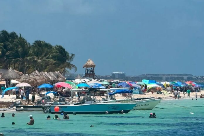 Embarcaciones y visitantes disfrutan de una playa con sombrillas y aguas turquesa en un destino turístico de Quintana Roo.