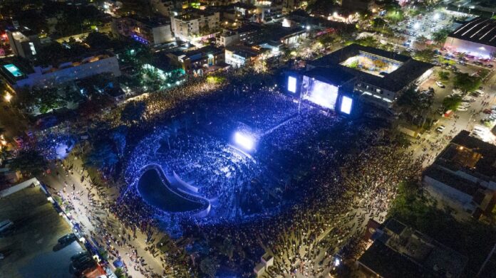 Vista aérea de un evento masivo en la Plaza 28 de Julio de Playa del Carmen con miles de asistentes reunidos frente al escenario.