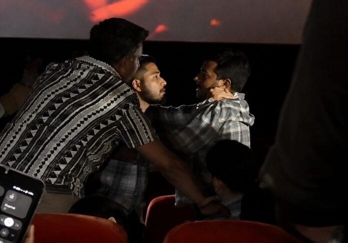 Dos hombres forcejean dentro de una sala de cine mientras otros asistentes intentan separarlos entre las filas de asientos.