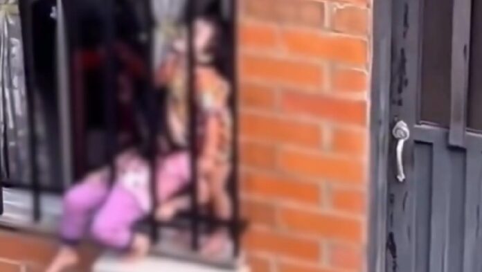 Dos niños permanecen entre la ventana y las rejas exteriores de una vivienda en Santa Rosa de Cabal, Colombia, antes de ser rescatados por las autoridades.