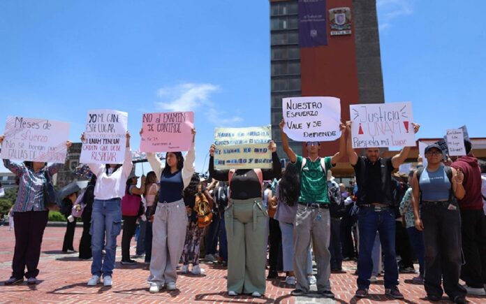 Aspirantes a la UNAM participan en una manifestación frente a instalaciones universitarias mientras sostienen carteles relacionados con el proceso de admisión.