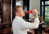 Luis Miguel reaparece con emotivo mensaje a México y desata debate sobre su identidad Luis Miguel sostiene una botella de refresco mientras bebe durante la grabación de un video promocional en un salón con mobiliario de madera.