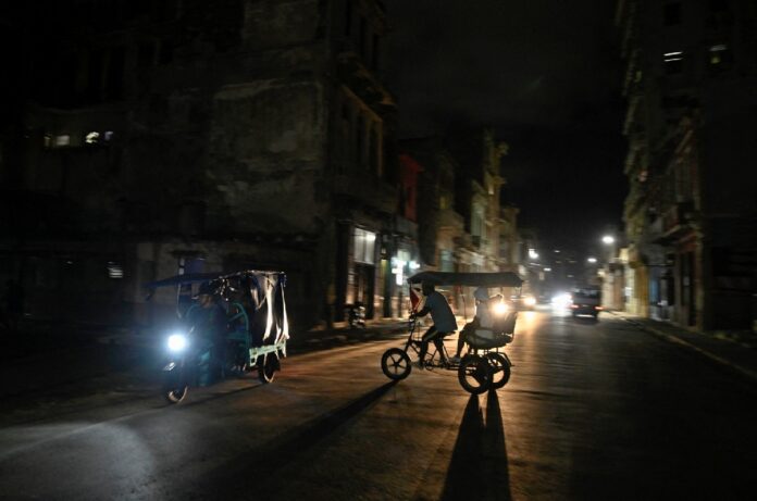 Dos bicitaxis circulan por una calle de La Habana durante la noche con escasa iluminación por un apagón eléctrico.