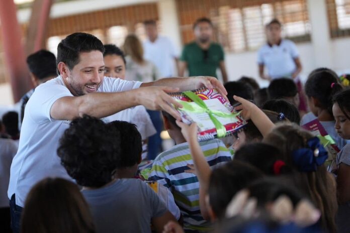 Renán Sánchez Tajonar entrega un kit de libretas a estudiantes durante una jornada de apoyo escolar en Cozumel.