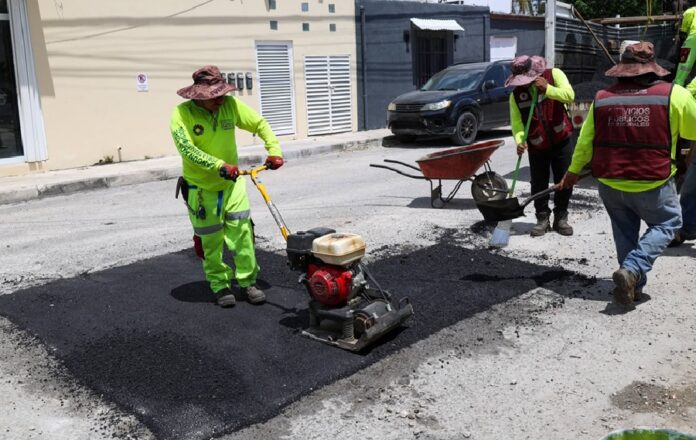 Trabajadores de Servicios Públicos Municipales realizan labores de bacheo en una calle de Cancún utilizando maquinaria compactadora.